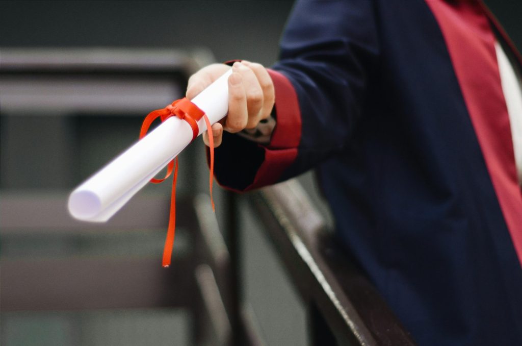 Image en gros plan d'un diplômé tenant son diplôme, noué avec un ruban rouge, symbole de réussite et de mérite.