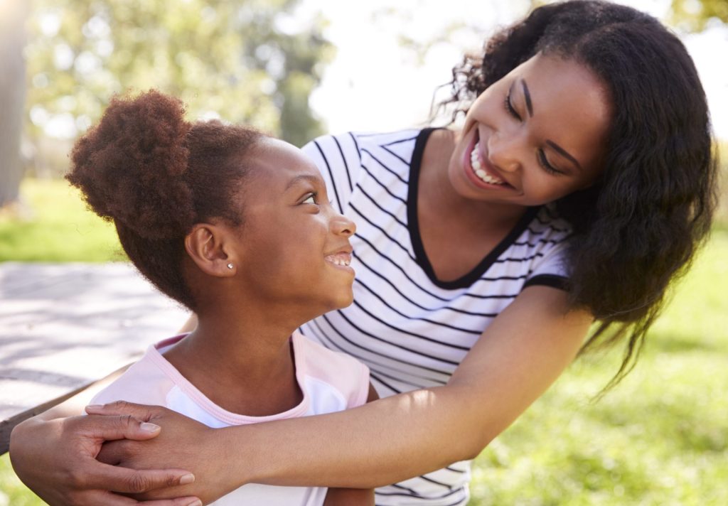 Une mère souriante prenant son enfant dans ses bras dans un parc, exprimant l’amour, la protection et la confiance.